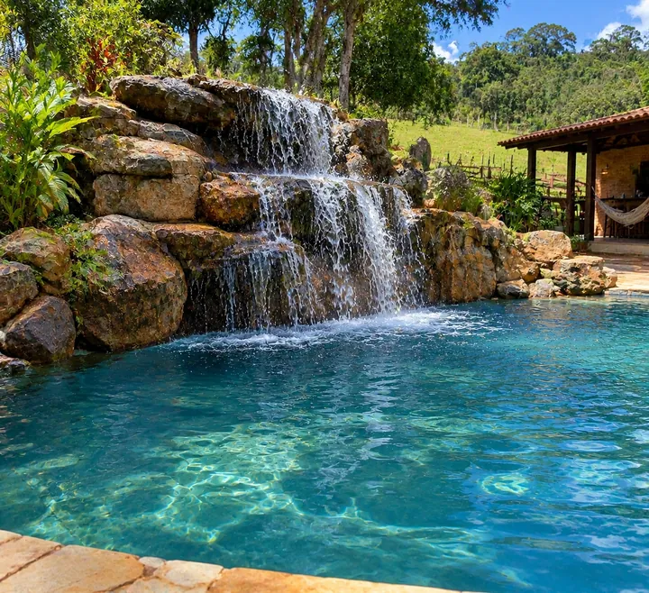 Piscina com cascata de grandes rochas em vários níveis junto a área de lazer com rede